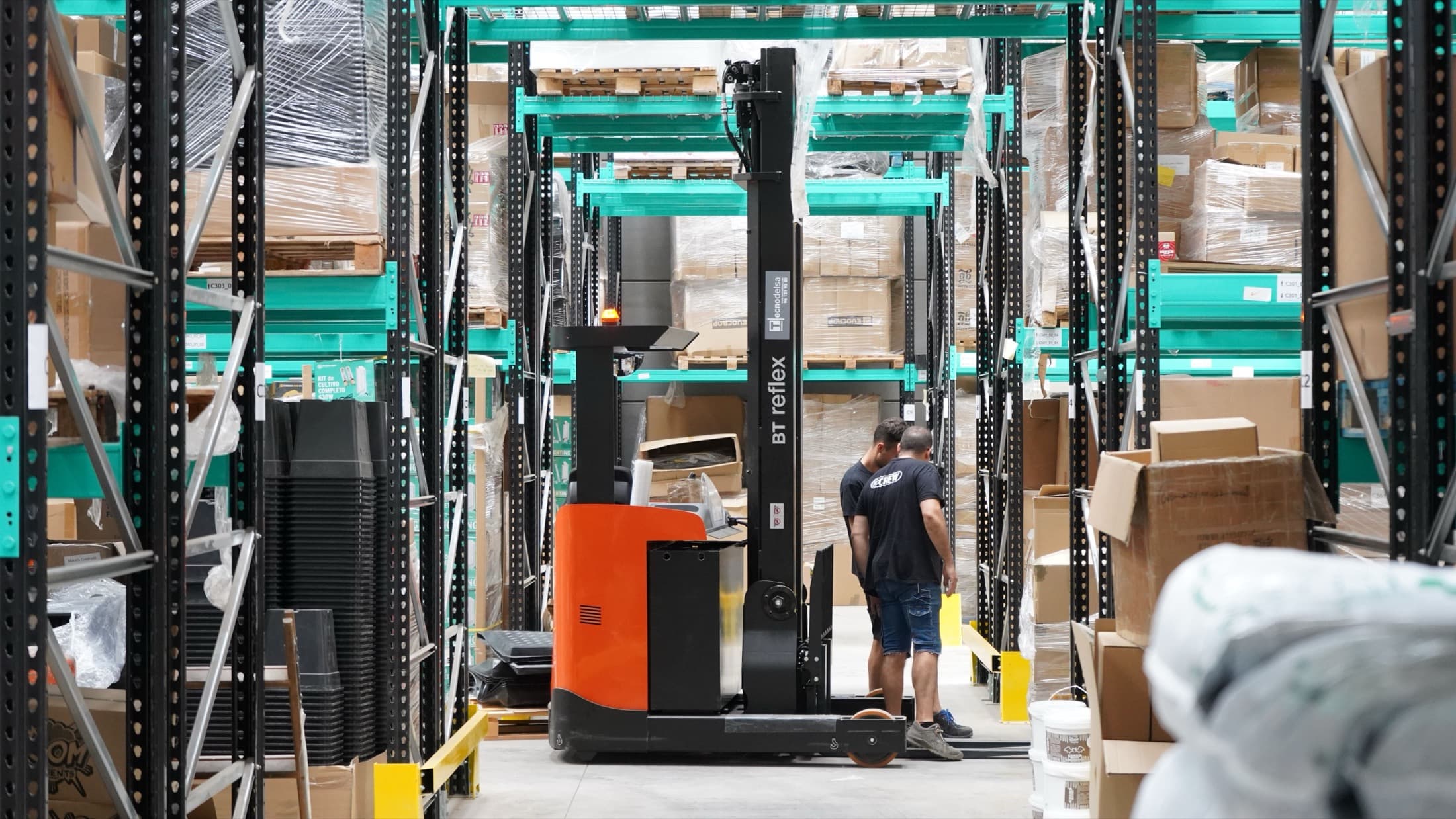 Workers and a forklift moving palletised goods in a large warehouse