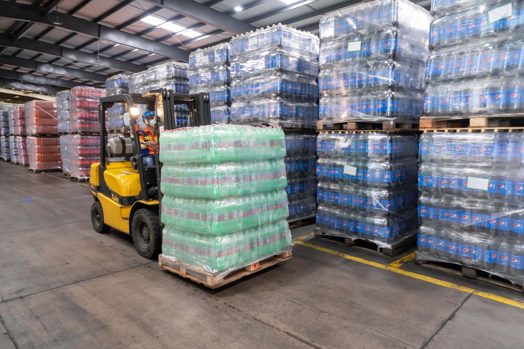 Forklift moving bottled-drink pallets inside a large distribution warehouse