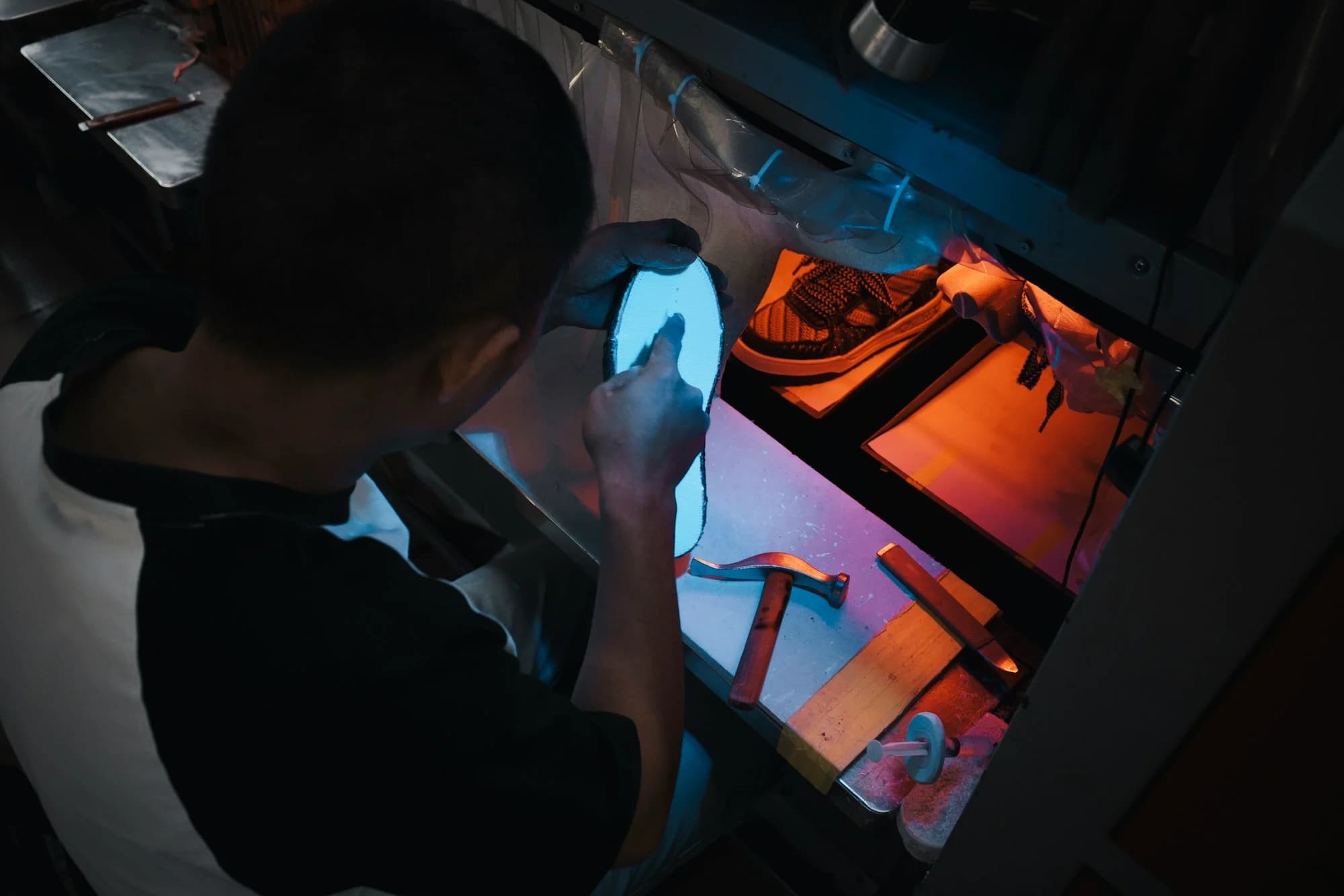 Worker handling a shoe at an illuminated industrial sole-processing station
