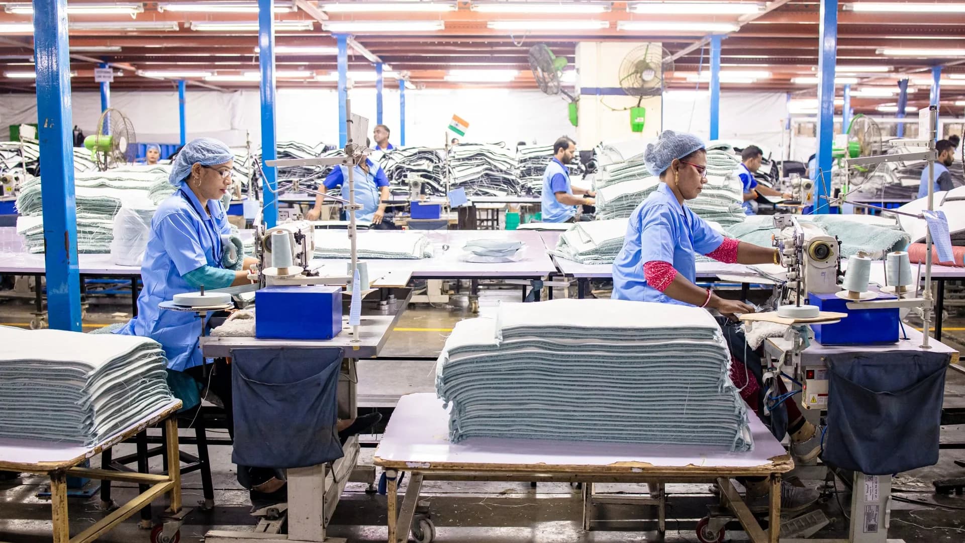 Large garment production floor in India with workers, industrial sewing machines and stacked cut pieces