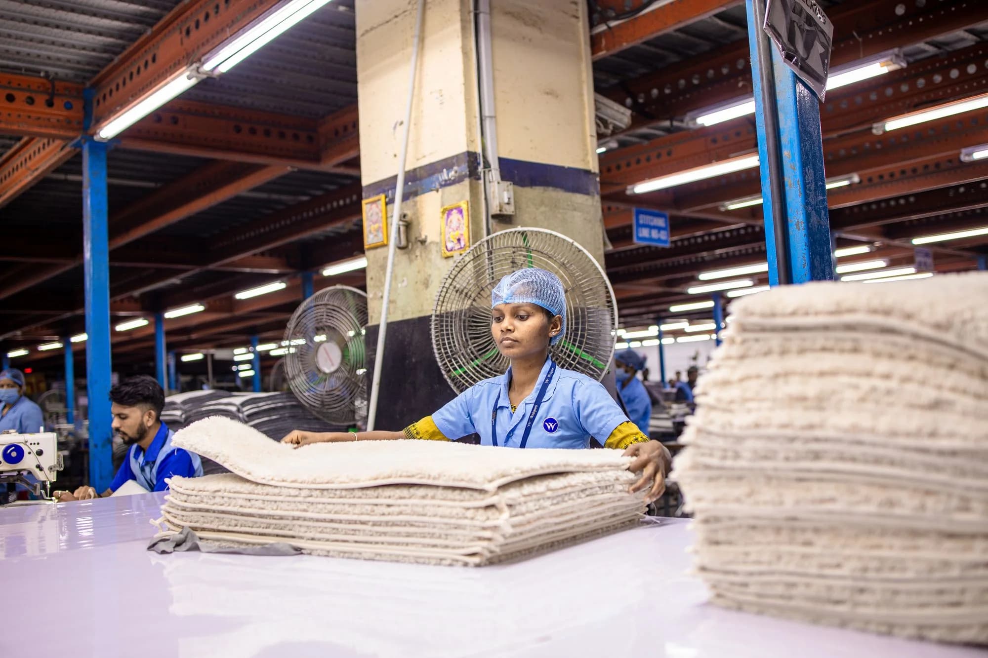 Workers sorting and organizing fabric rolls on a large textile factory floor in India