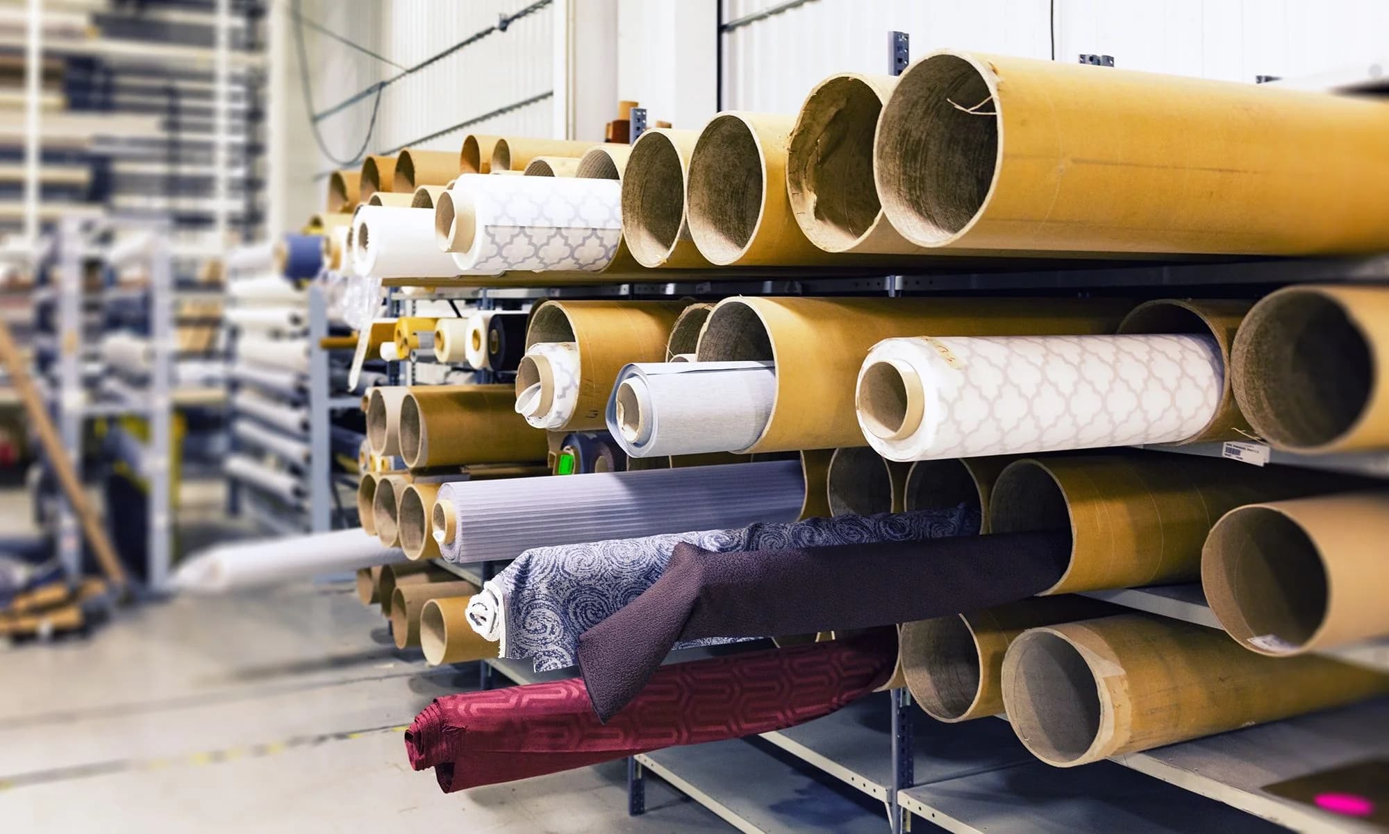 Rows of textile rolls stored on racks inside a large industrial fabric warehouse